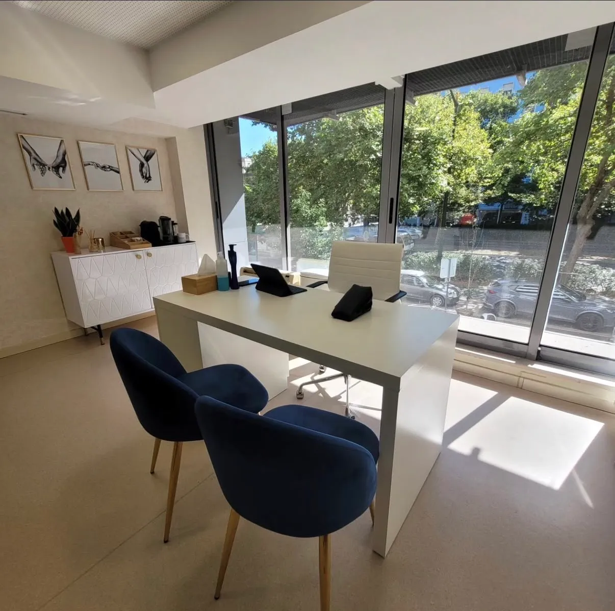 Sala de consulta com secretária, duas cadeiras azuis e janelas amplas