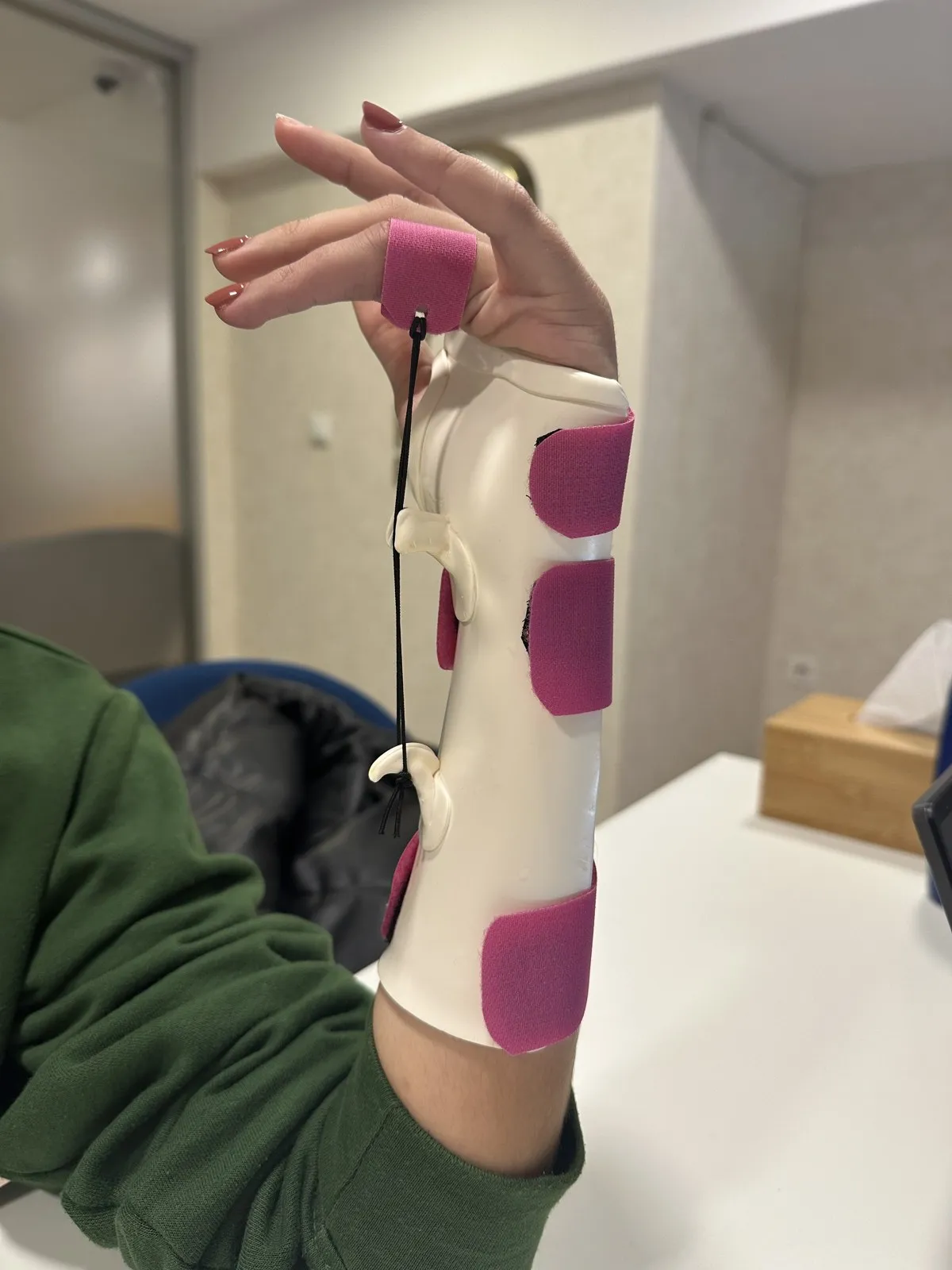 Ortótese branca de punho com almofadas rosa e um fio de tração até um dedo